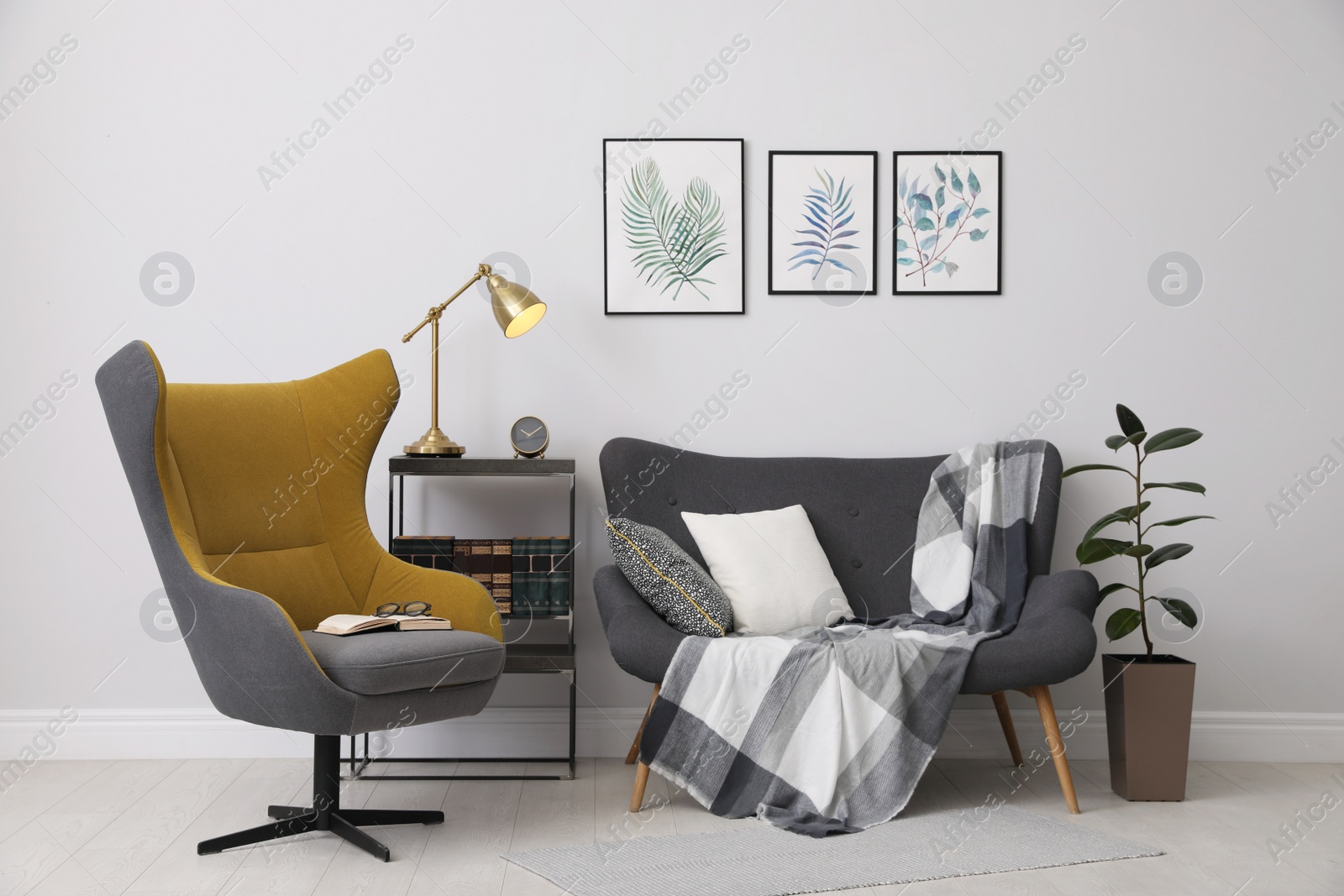 Photo of Stylish room interior with comfortable armchair, sofa and paintings of tropical leaves