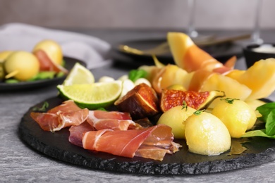 Photo of Slate plate with melon slices and prosciutto on table