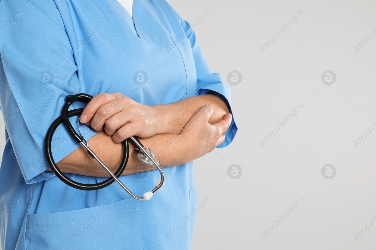 Photo of Mature doctor with stethoscope on light grey background, closeup. Space for text