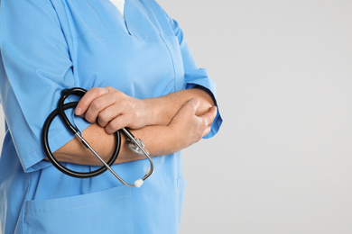 Mature doctor with stethoscope on light grey background, closeup. Space for text