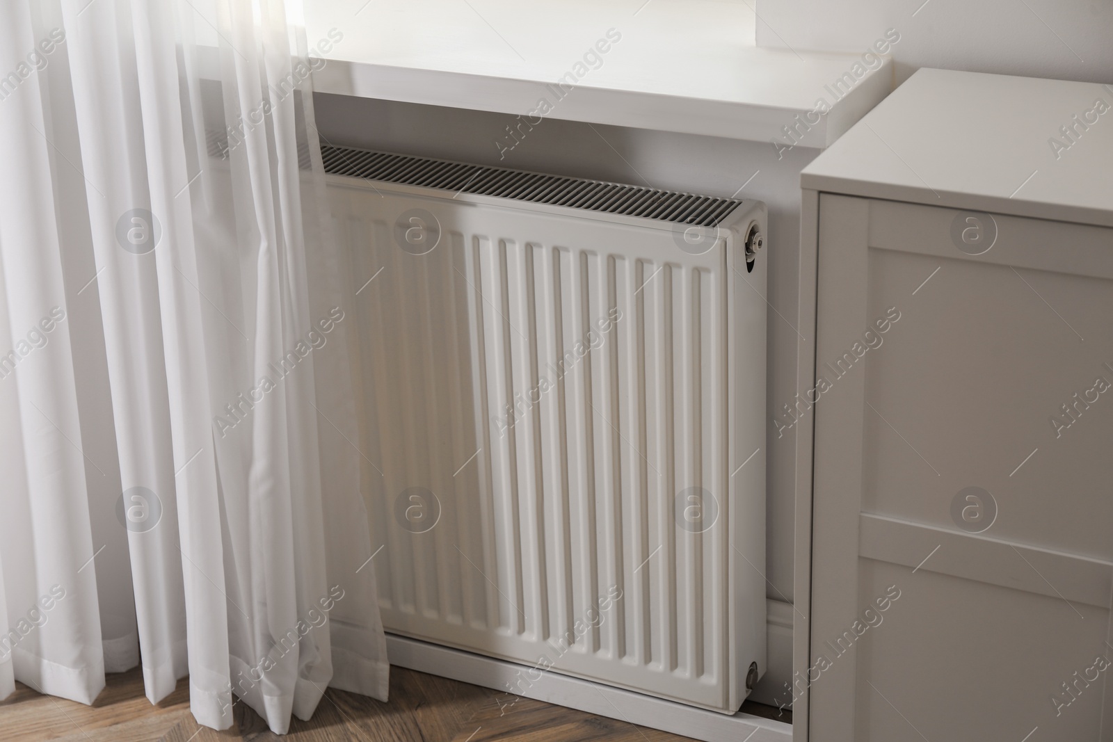 Photo of Modern radiator on white wall near window indoors