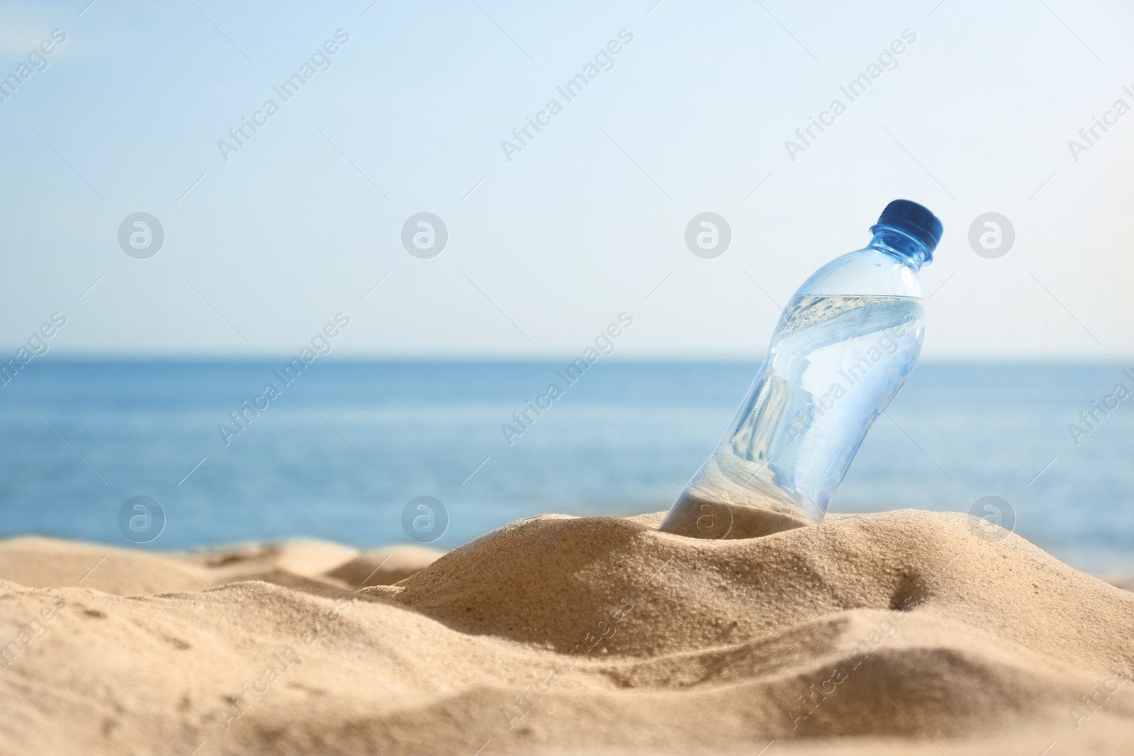 Photo of Sandy beach with bottle of refreshing drink on hot summer day, space for text
