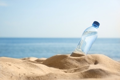 Photo of Sandy beach with bottle of refreshing drink on hot summer day, space for text