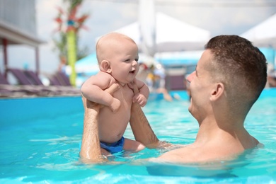 Photo of Man with his little baby in swimming pool on sunny day, outdoors