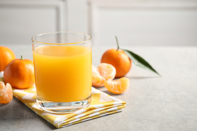 Photo of Glass of fresh tangerine juice and fruits on light grey table. Space for text