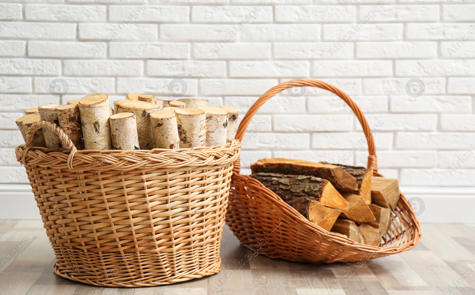 Photo of Wicker baskets with firewood near white brick wall indoors