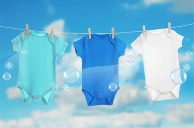 Image of Colorful baby onesies hanging on clothes line and washing powder bubbles against cloudy sky