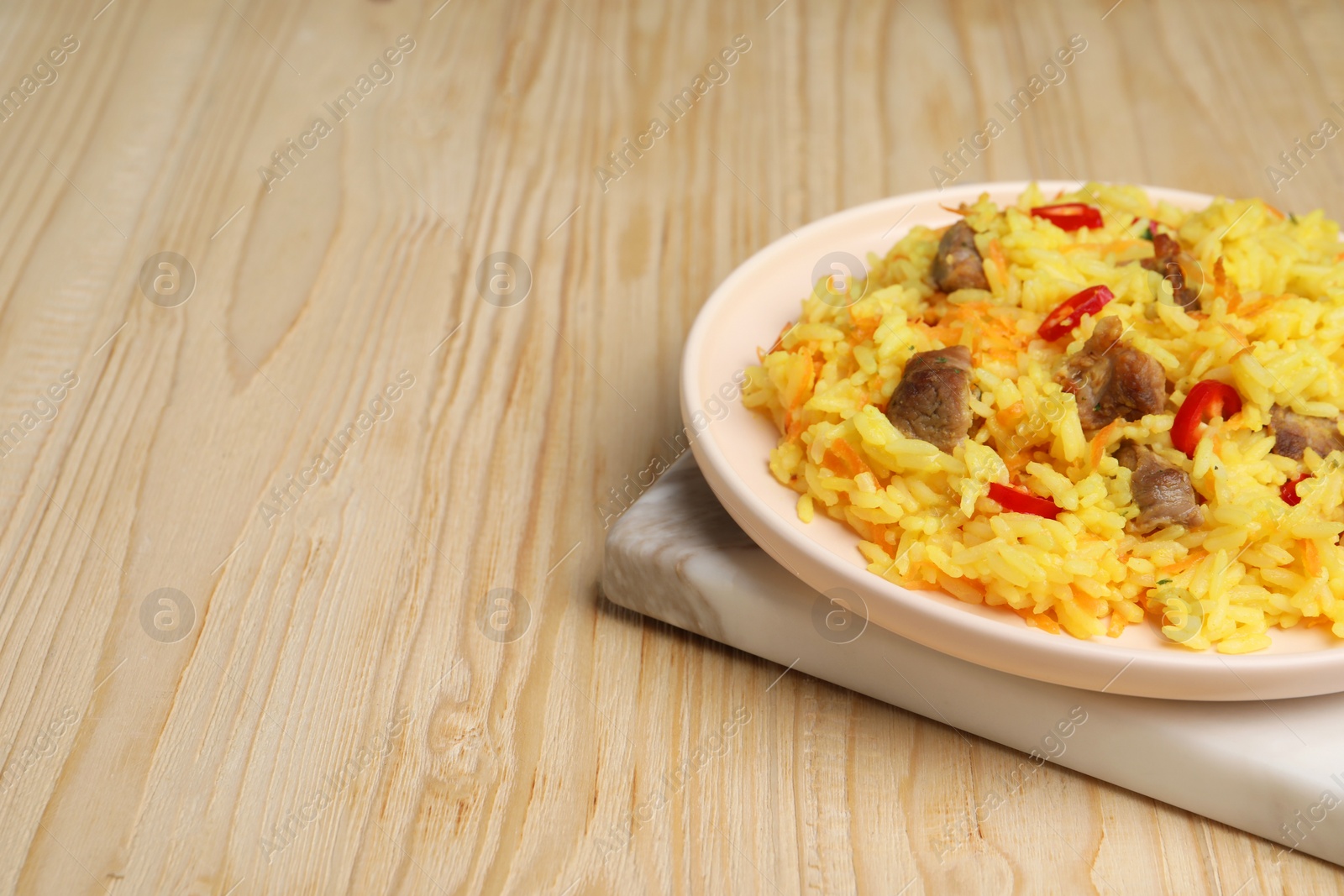 Photo of Delicious pilaf with meat on wooden table. Space for text