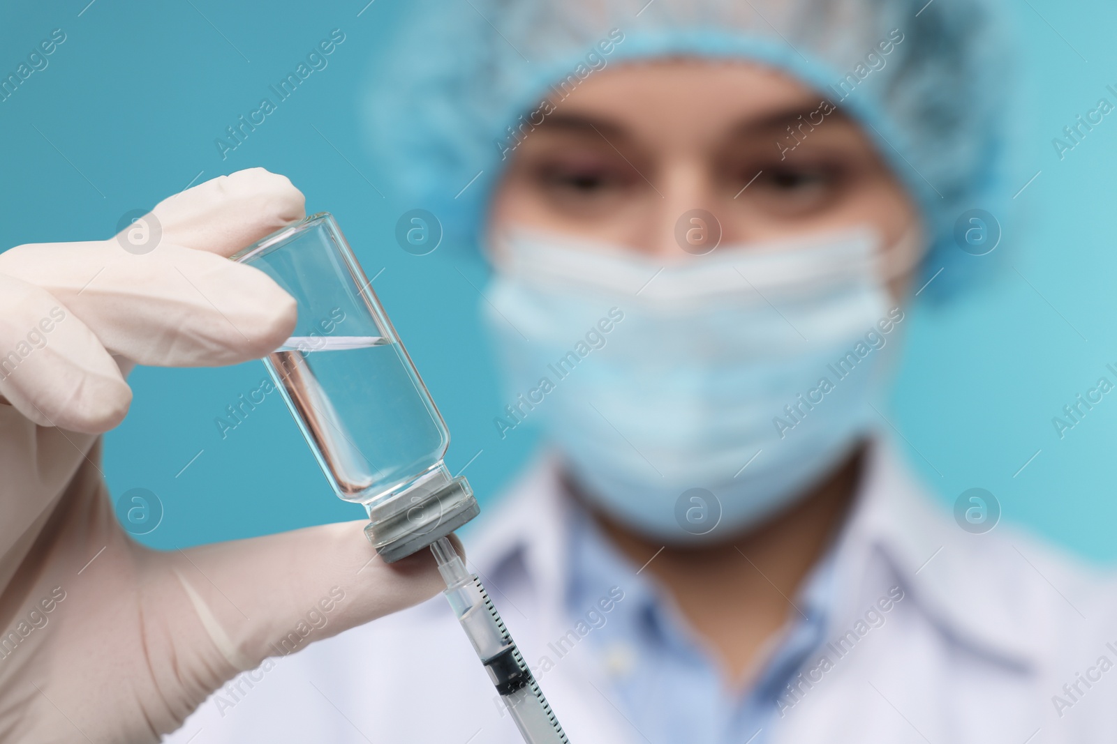 Photo of Doctor filling syringe with medication from glass vial on light blue background, selective focus