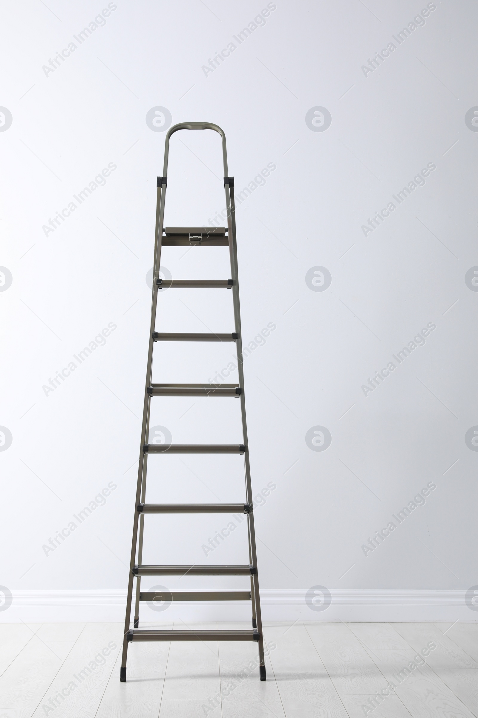 Photo of Modern metal stepladder near white wall indoors