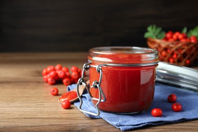 Photo of Delicious rowan jam in jar on wooden table. Space for text