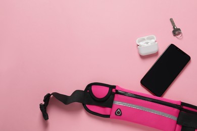 Photo of Stylish waist bag with smartphone, key and earphones on pink background, flat lay. Space for text