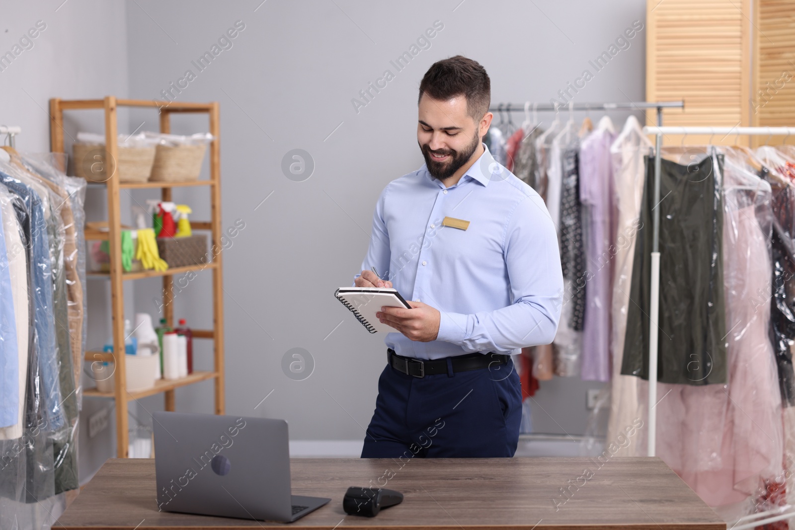 Photo of Dry-cleaning service. Happy worker taking notes in workplace indoors