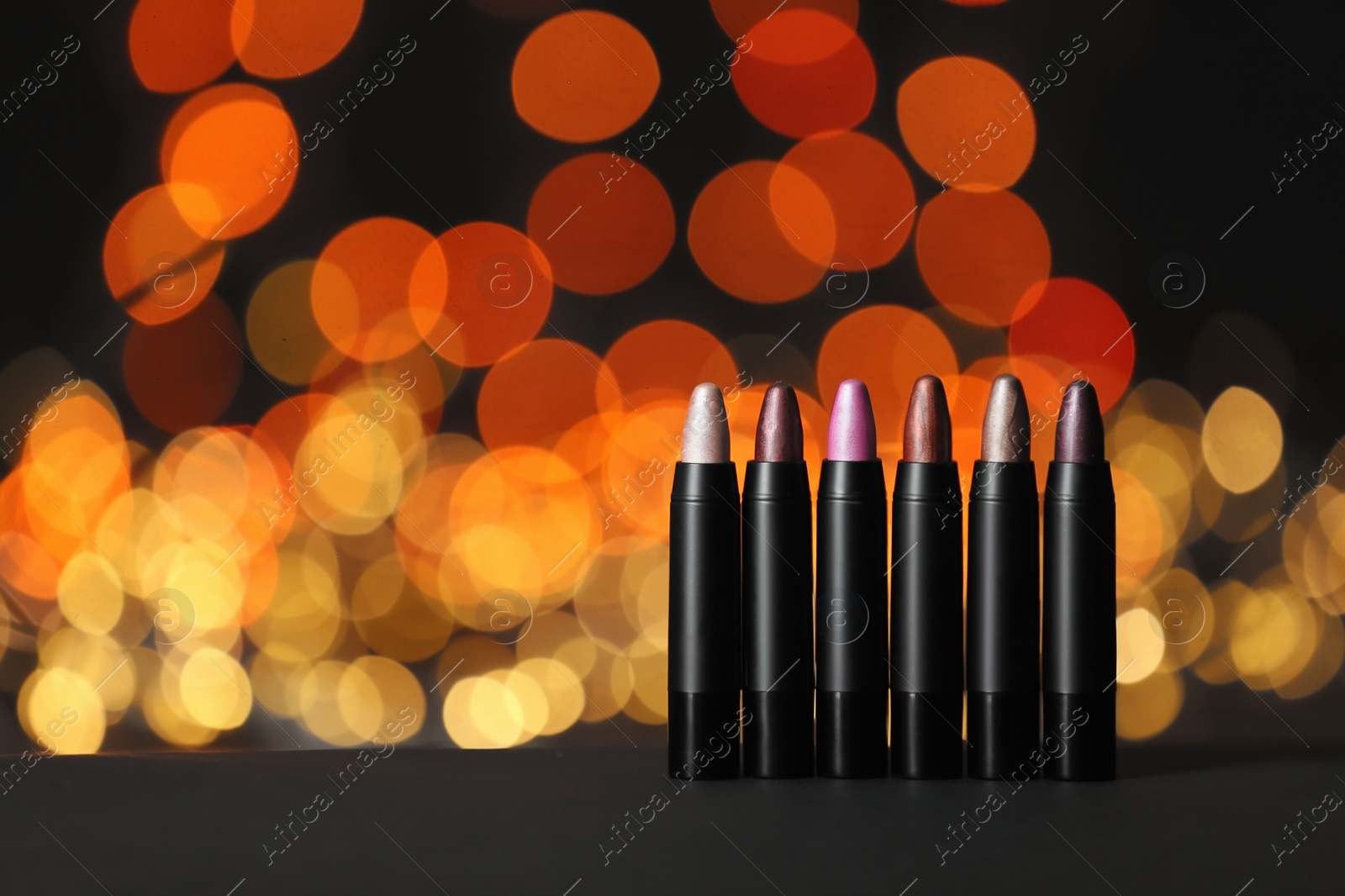 Photo of Set of bright lipsticks on table against blurred lights, space for text