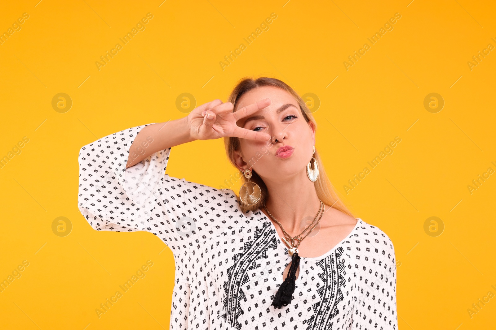 Photo of Portrait of hippie woman showing peace sign on yellow background