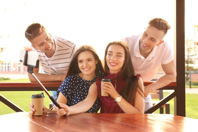 Photo of Group of young people taking selfie with monopod in gazebo on sunny day