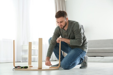 Photo of Young working man repairing table at home