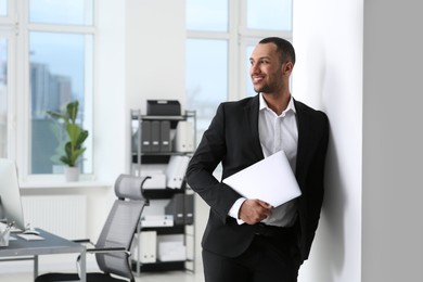 Photo of Smiling young businessman with laptop in modern office. Space for text