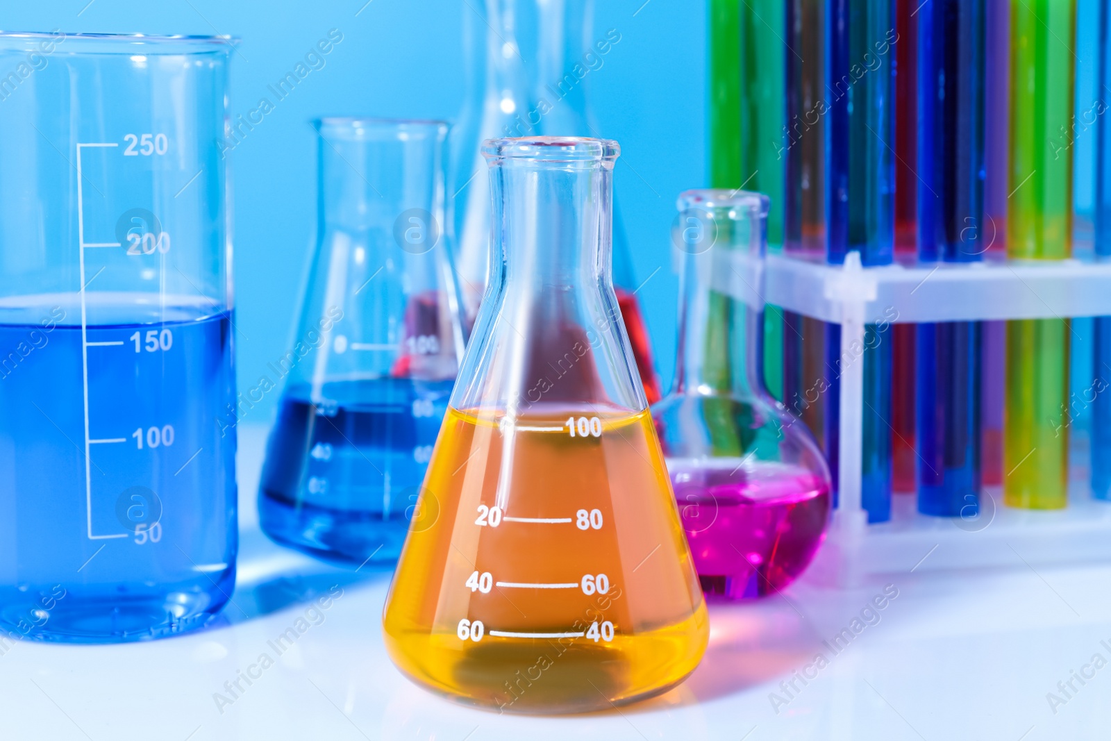 Photo of Different laboratory glassware with colorful liquids on white table against light blue background