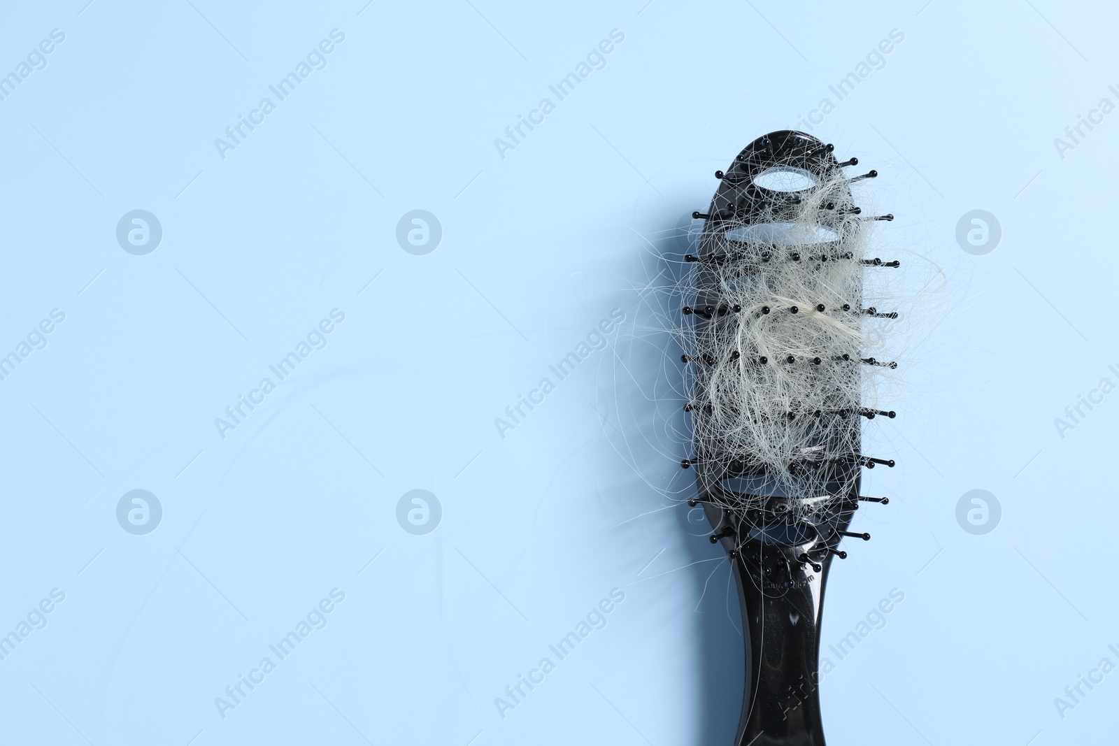 Photo of Brush with lost hair on light blue background, top view. Space for text