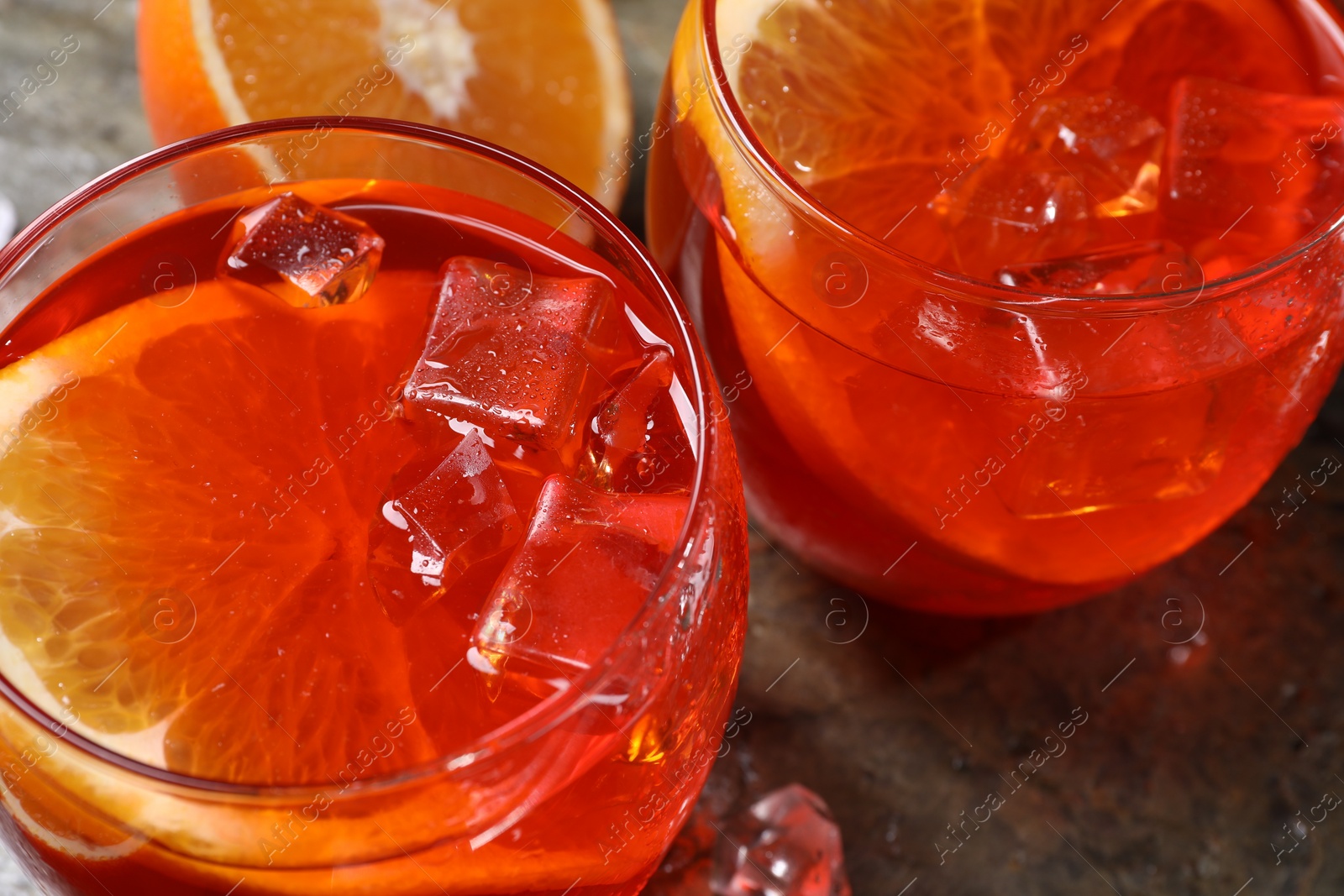 Photo of Aperol spritz cocktail, ice cubes and orange slices in glasses on grey textured table, closeup