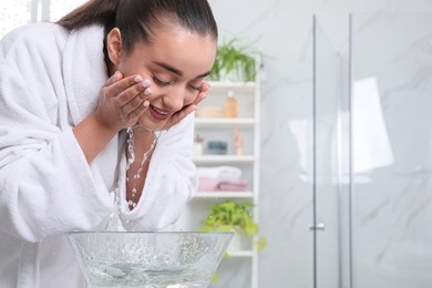 Beautiful young woman washing her face with water in bathroom, space for text