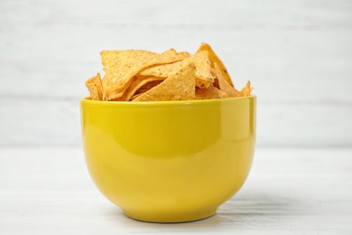 Photo of Yellow bowl with tasty Mexican nachos chips on white wooden table