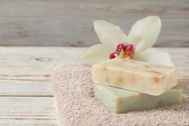Photo of Soap bars, terry towel and lily on wooden table, closeup. Space for text