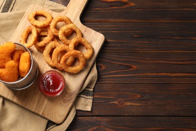 Photo of Board with tasty ketchup, chicken nuggets and onion rings on wooden table, top view. Space for text