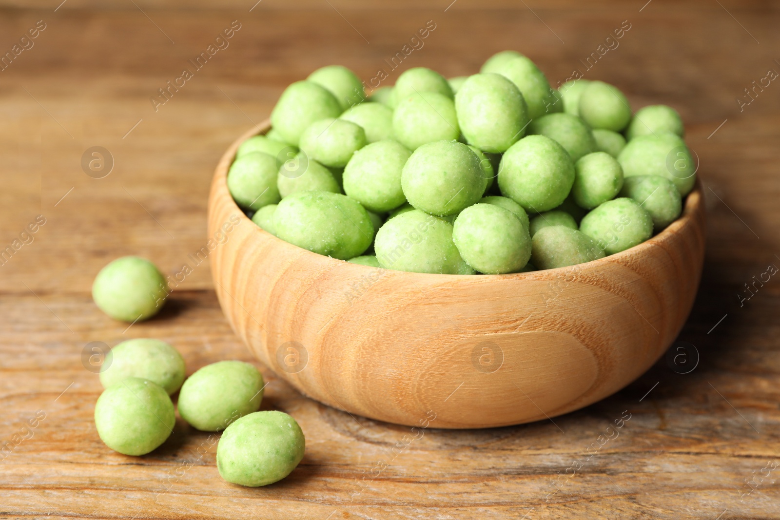 Photo of Tasty wasabi coated peanuts on brown wooden table, closeup