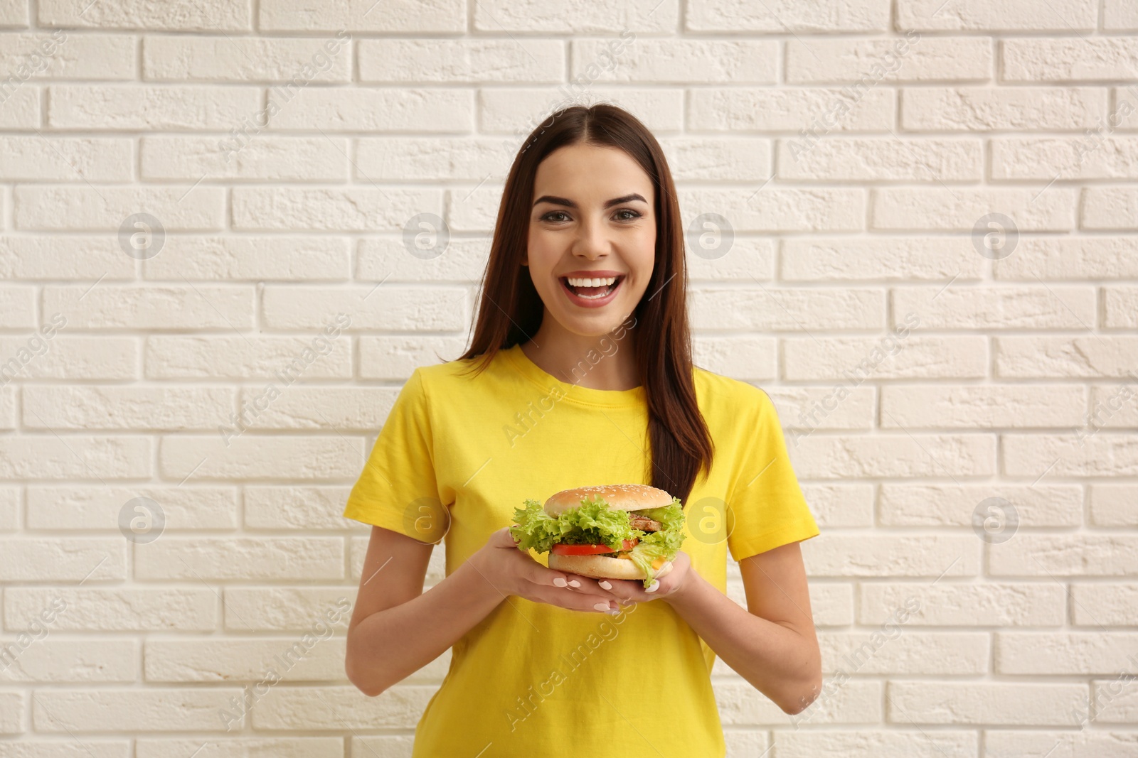 Photo of Young woman with tasty burger near brick wall