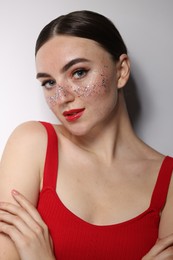 Beautiful woman with glitter freckles on light background