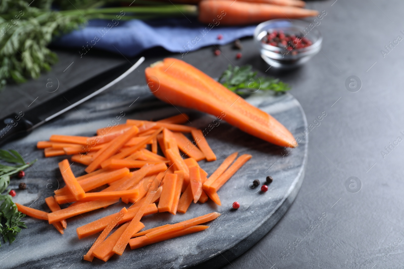 Photo of Cut raw carrot and marble board on grey table, closeup