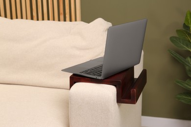 Photo of Laptop on sofa armrest wooden table in room. Interior element