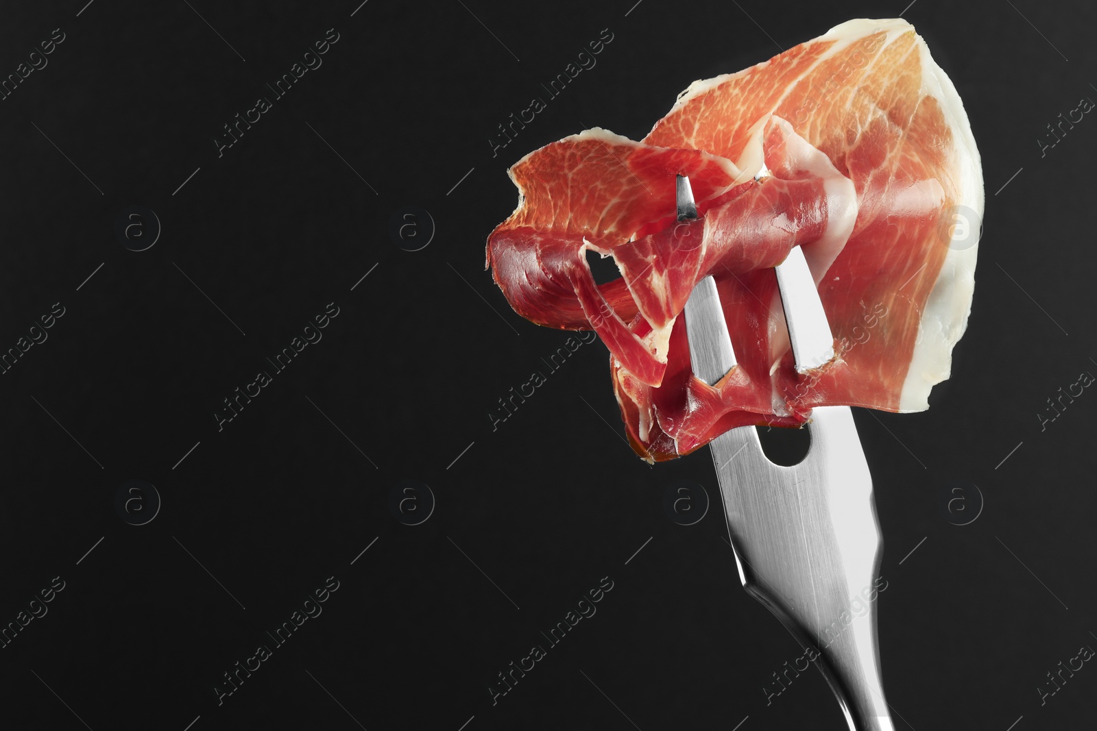 Photo of Fork with slice of tasty jamon on black background, closeup. Space for text