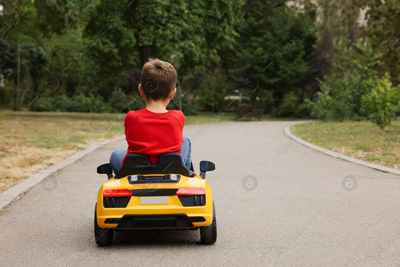 Photo of Cute little boy driving children's car outdoors, back view. Space for text