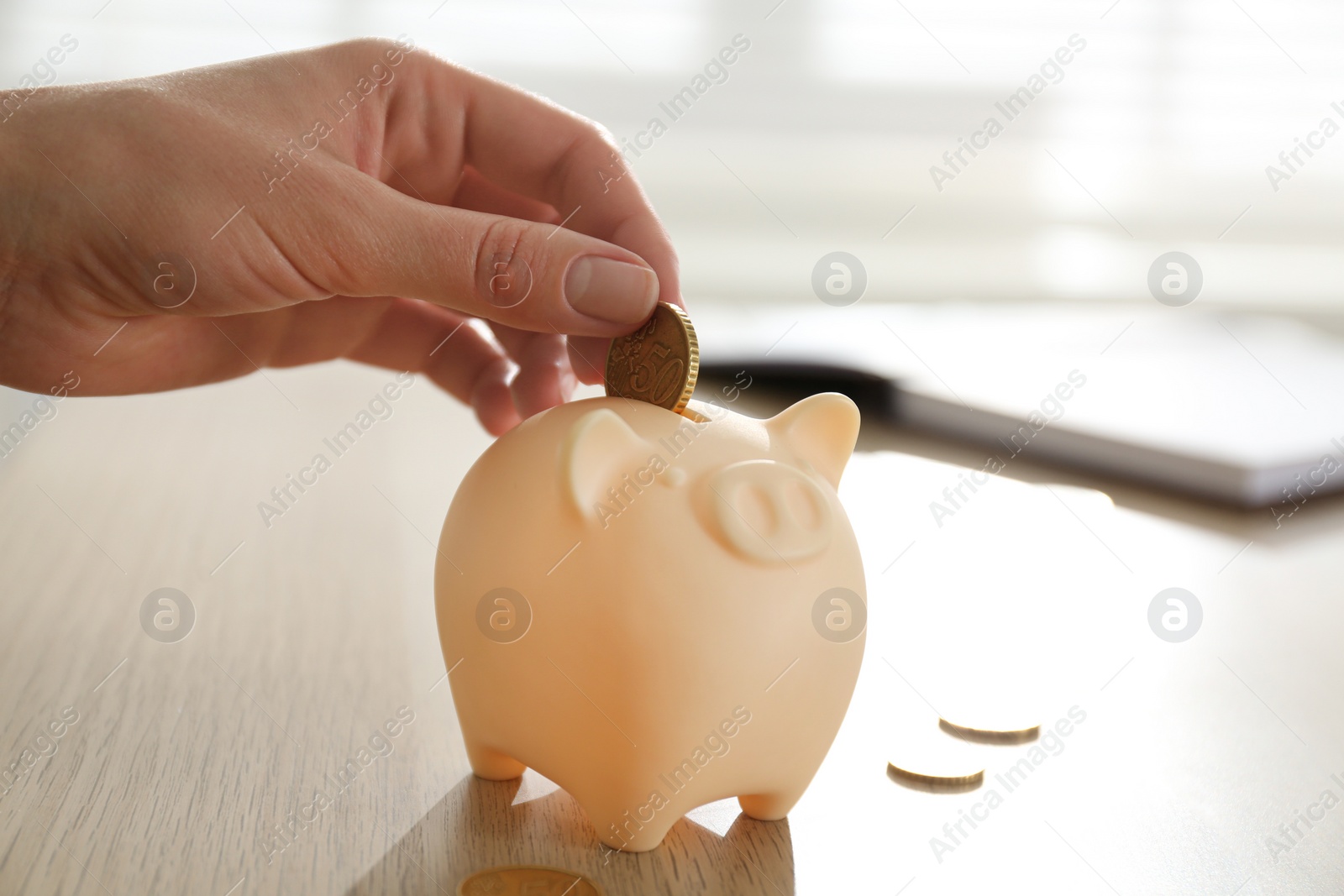 Photo of Woman putting money into piggy bank at wooden table indoors, closeup