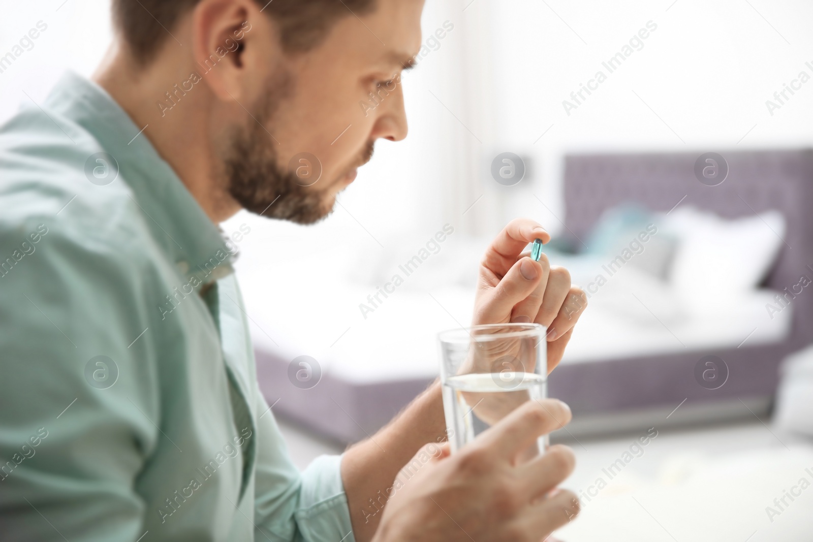 Photo of Young man with pill and glass of water indoors