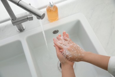 Woman washing hands with liquid soap at home, closeup