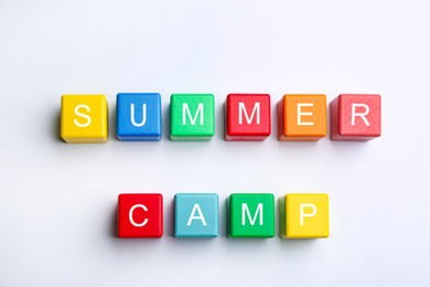 Colorful wooden cubes with phrase SUMMER CAMP on white background, top view