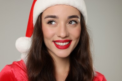 Photo of Christmas celebration. Beautiful young woman in Santa hat on grey background, closeup