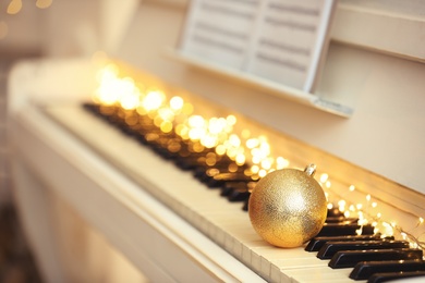 Photo of Beautiful golden bauble and fairy lights on piano keys, space for text. Christmas music