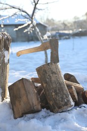Metal axe in wooden log and pile of wood outdoors on sunny winter day