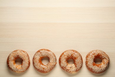 Photo of Delicious fresh bagels with sesame seeds on light wooden table, flat lay. Space for text