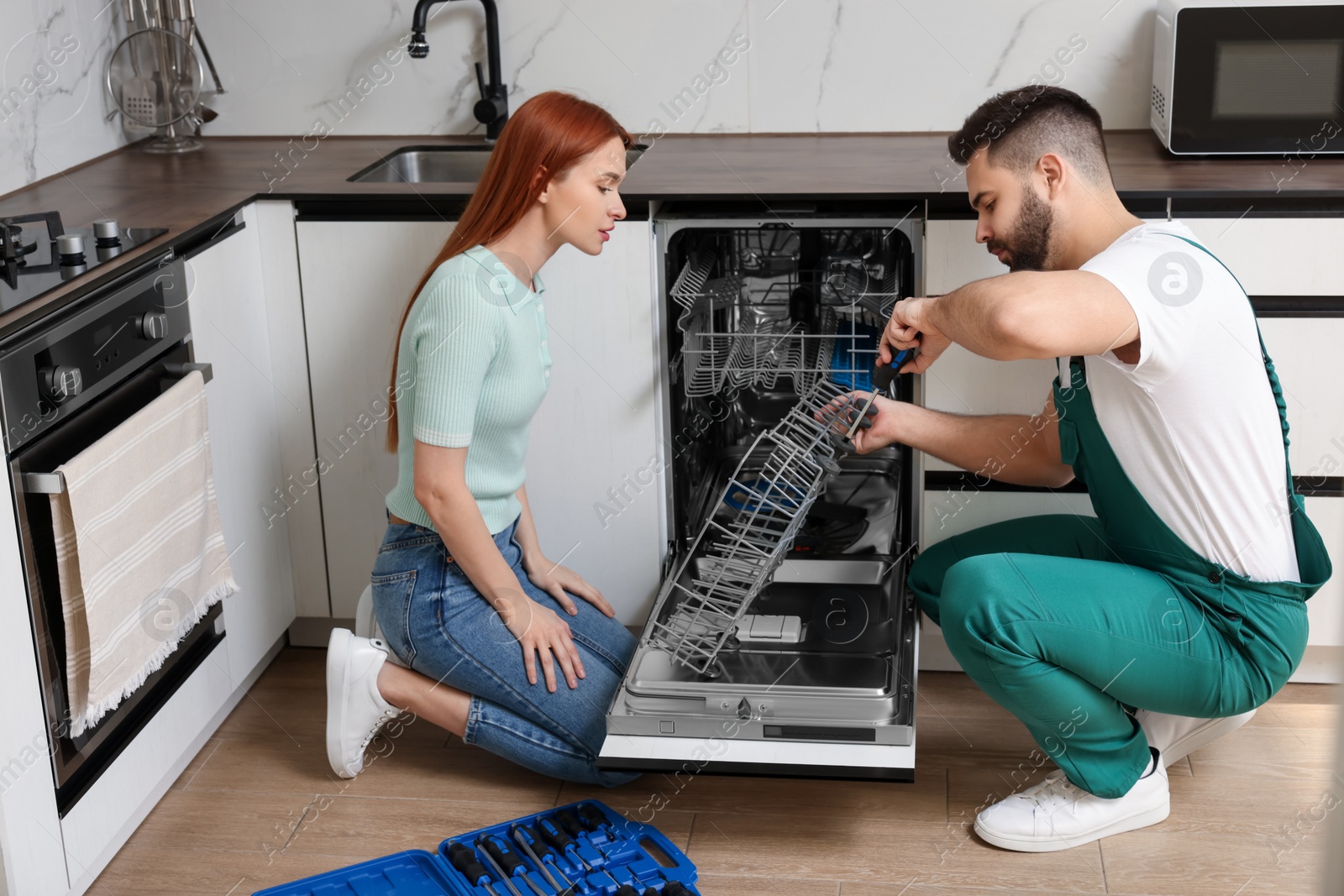 Photo of Woman looking how serviceman repairing her dishwasher in kitchen