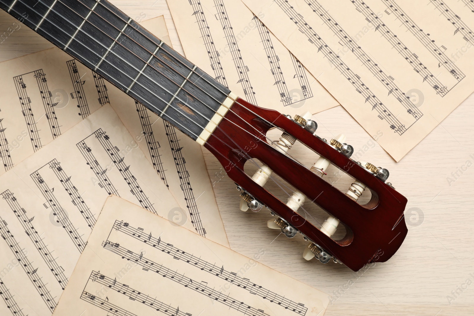 Photo of Composition with guitar and music notations on light wooden table, flat lay