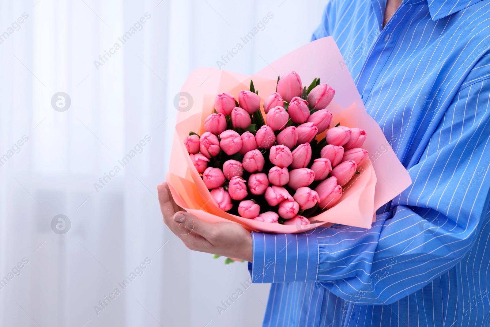 Photo of Woman holding bouquet of pink tulips indoors, closeup. Space for text