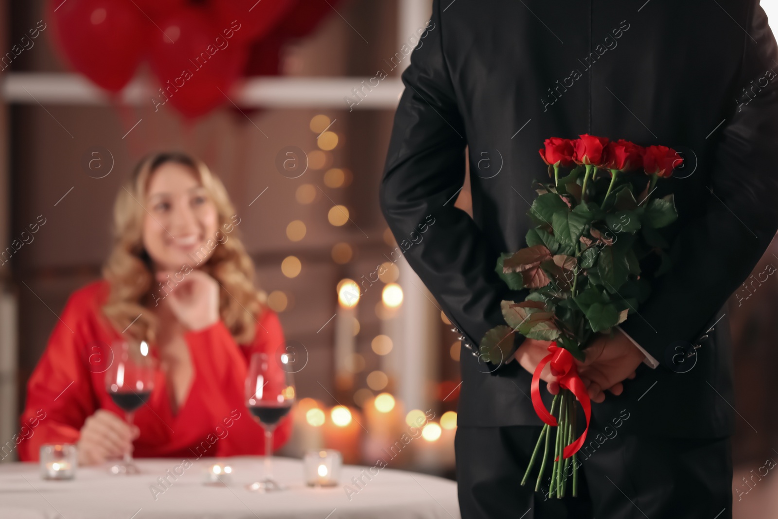 Photo of Man hiding roses for his beloved woman in restaurant at Valentine's day dinner