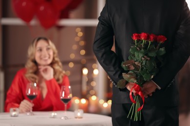 Photo of Man hiding roses for his beloved woman in restaurant at Valentine's day dinner