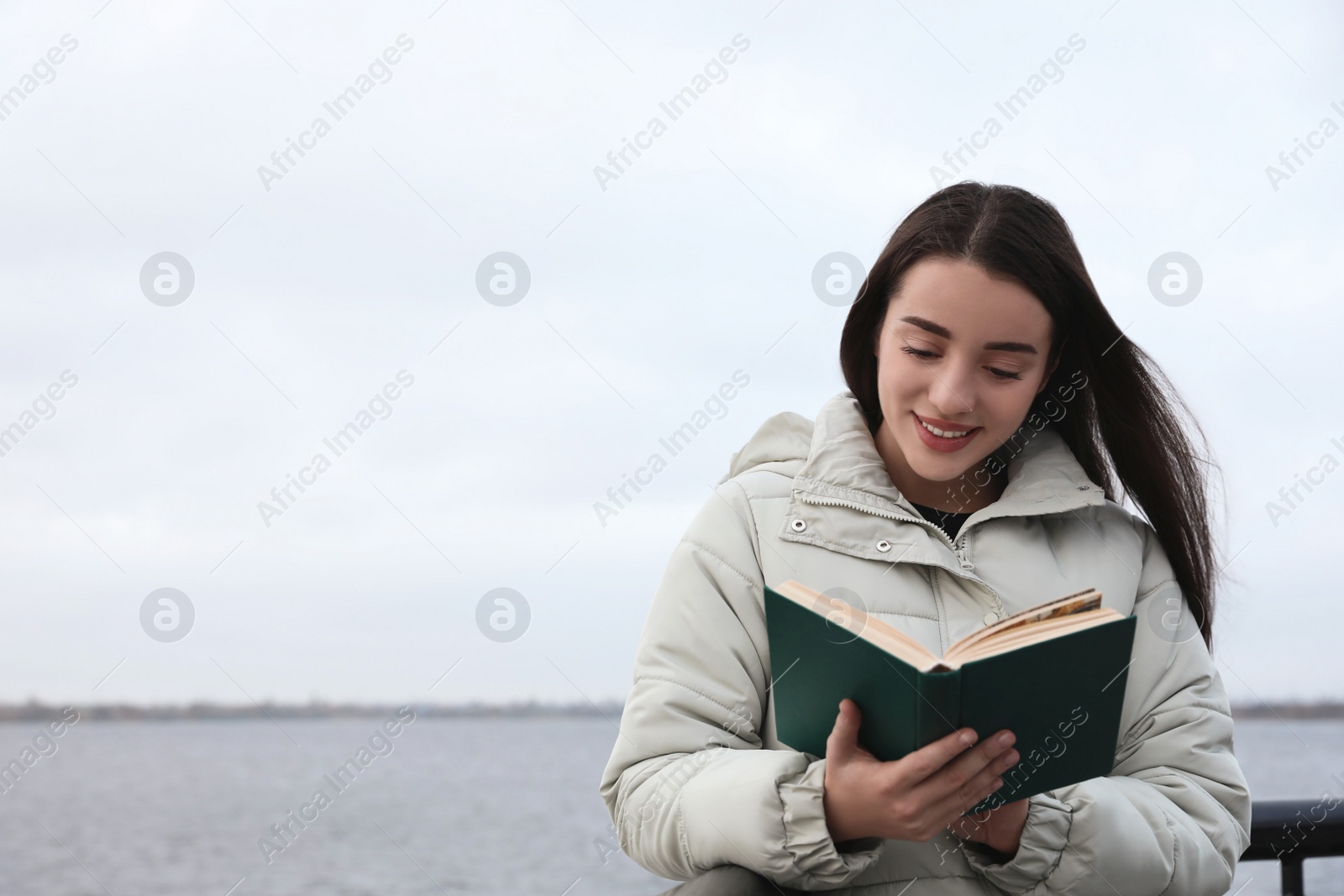 Photo of Woman reading book near river on cloudy day